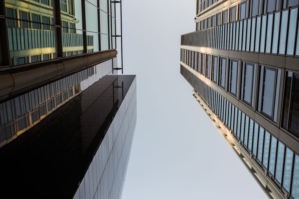 Upward view between modern commercial buildings with glass windows and contemporary architecture.