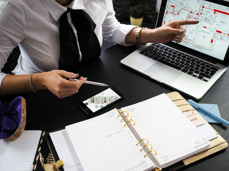 Professional reviewing a project on a laptop while using a planner and mobile device for business and website planning.