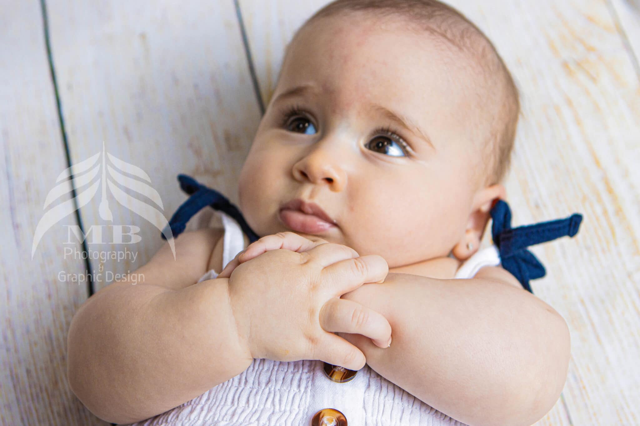 Photography Portfolio 38 Mariam Cheaitou Bazzi Photography Portfolio in Windsor Close-up portrait of a baby with hands gently clasped, wearing a white outfit with navy blue accents during a milestone photography session in Windsor, Ontario.