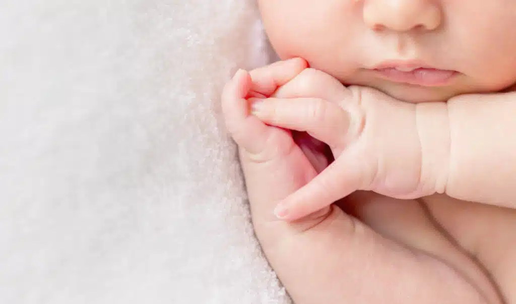 Tender lips and nose and crossed fingers of a newborn baby asleep.