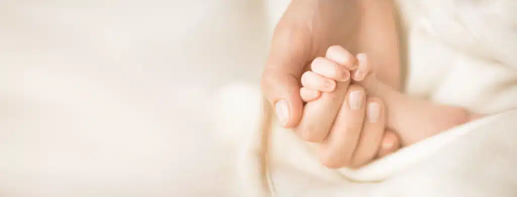 Female hand holding her newborn baby's hand. 