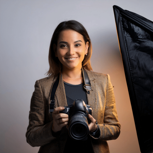 Smiling woman in blazer holding a DSLR camera in a studio with softbox lighting