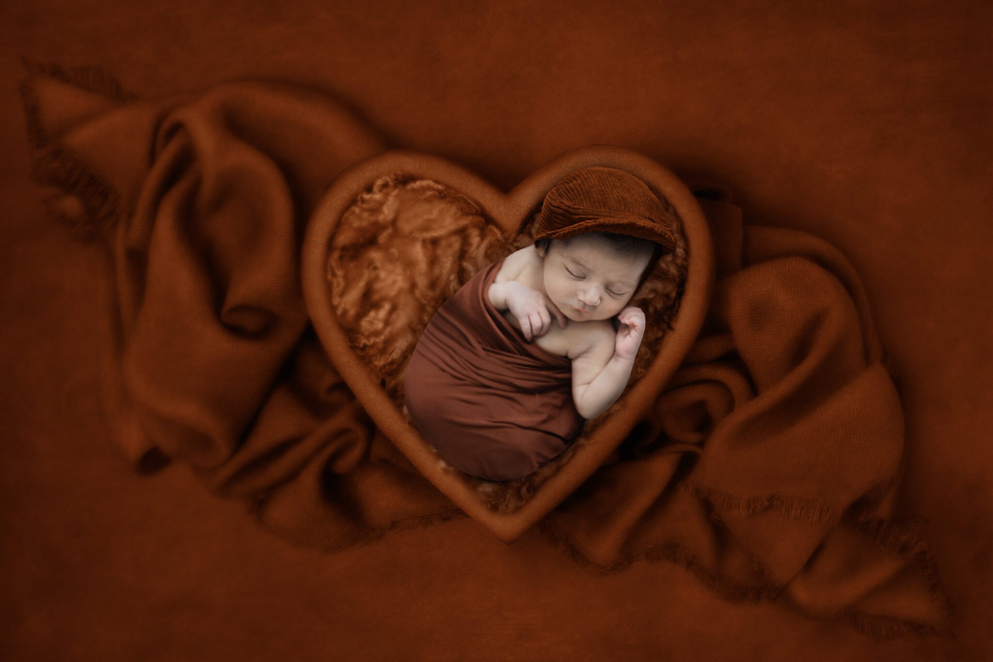 Photography Portfolio 25 Mariam Cheaitou Bazzi Photography Portfolio in Windsor Newborn baby swaddled in heart-shaped bowl on rich brown digital composite background, creative newborn photography by Windsor Ontario photographer