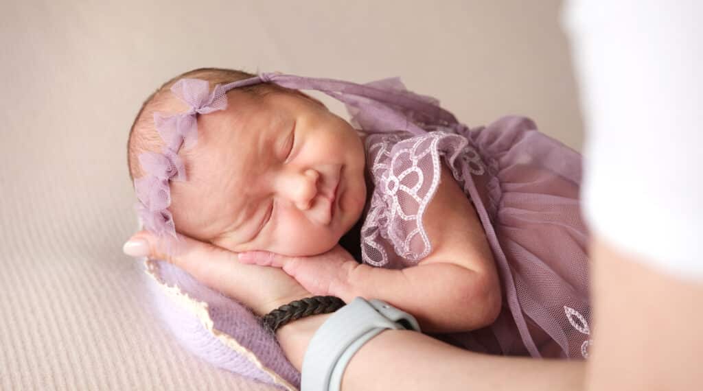 Newborn photographer cradling adorable Newborn Baby Girl In Wreath In Her Arms.