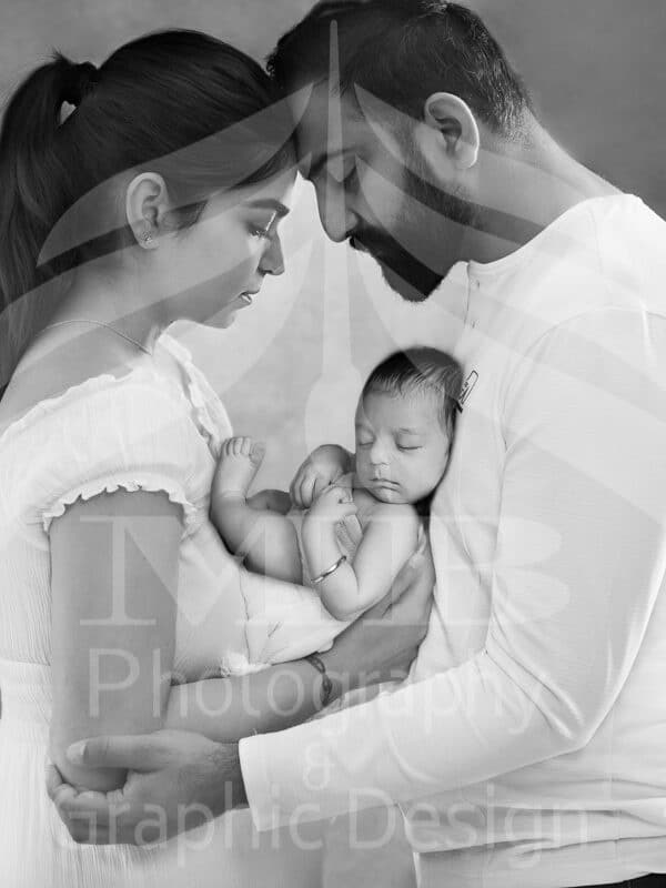 Photography Portfolio 56 Mariam Cheaitou Bazzi Photography Portfolio in Windsor Black and white portrait of mother and father gently holding their sleeping newborn baby during a warm studio family photography session in Windsor, Ontario.