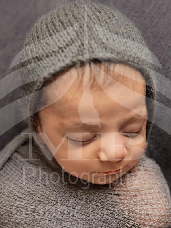 Photography Portfolio 19 Mariam Cheaitou Bazzi Photography Portfolio in Windsor Close-up of swaddled sleeping newborn baby wearing grey knit bonnet, professional newborn photography by Windsor Ontario photographer