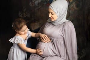 Photography Portfolio 28 Mariam Cheaitou Bazzi Photography Portfolio in Windsor Young daughter gently touching her pregnant mother’s belly during a studio maternity photography session in Windsor, Ontario.
