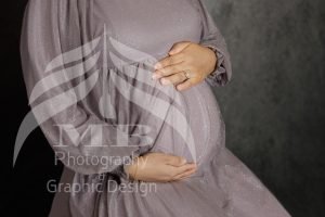 Photography Portfolio 27 Mariam Cheaitou Bazzi Photography Portfolio in Windsor Close-up of an expectant mother gently holding her baby bump while wearing a soft grey maternity gown during a studio session in Windsor, Ontario.