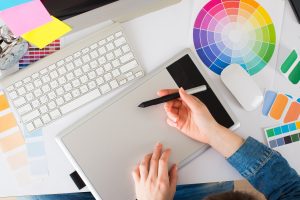 Graphic designer using a digital drawing tablet beside a keyboard, colour wheel and printed colour swatches in Windsor, Ontario.