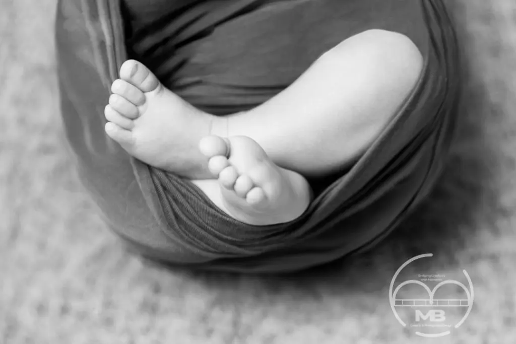 Black and white newborn photography in Windsor, Ontario featuring a close-up of a baby’s feet wrapped in a soft fabric, captured in a minimal and timeless studio style by MB Graphic & Photography Design.